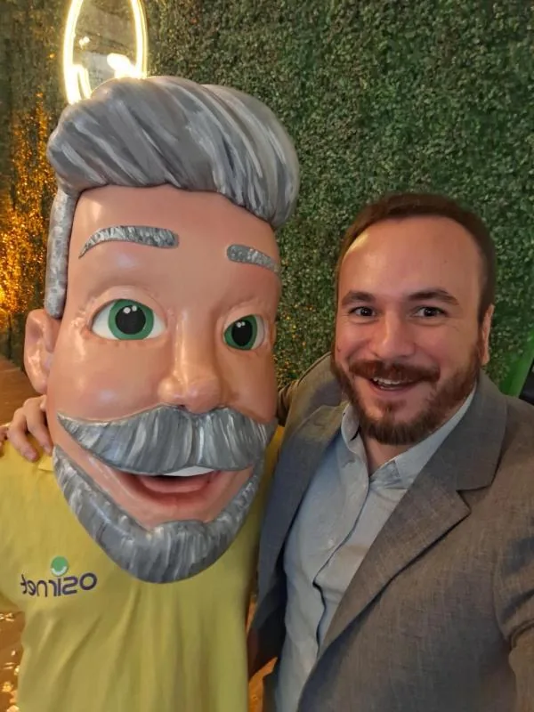 Homem ao lado de busto caricato em evento da Osirnet